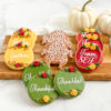 Assorted decorated Thanksgiving sugar cookies featuring autumn-colored icing, festive text like "Gather" and "Thankful," floral piping accents, and a turkey-shaped cookie, set on a wooden platter alongside mini white pumpkins.