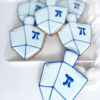 write alt text Dreidel-shaped sugar cookies decorated with light blue and white icing, dark blue outlines, and the Hebrew letter He in the center.