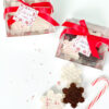 [Snowflake-shaped chocolates and peppermint barks packaged in clear gift boxes tied with red ribbons, displayed alongside loose snowflake treats, candy canes, and peppermint sprinkles]