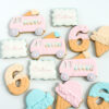 Hand-decorated pastel sugar cookies shaped like ice cream trucks, waffle cones, and number six cookies, with personalized name plaques , arranged on a light background.