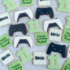 Video Game-theme birthday cookies black gaming controller, white and black gaming controller, number cookie with green pixelated design, square bruh cookie with gaming controllers background and happy birthday cookie and name