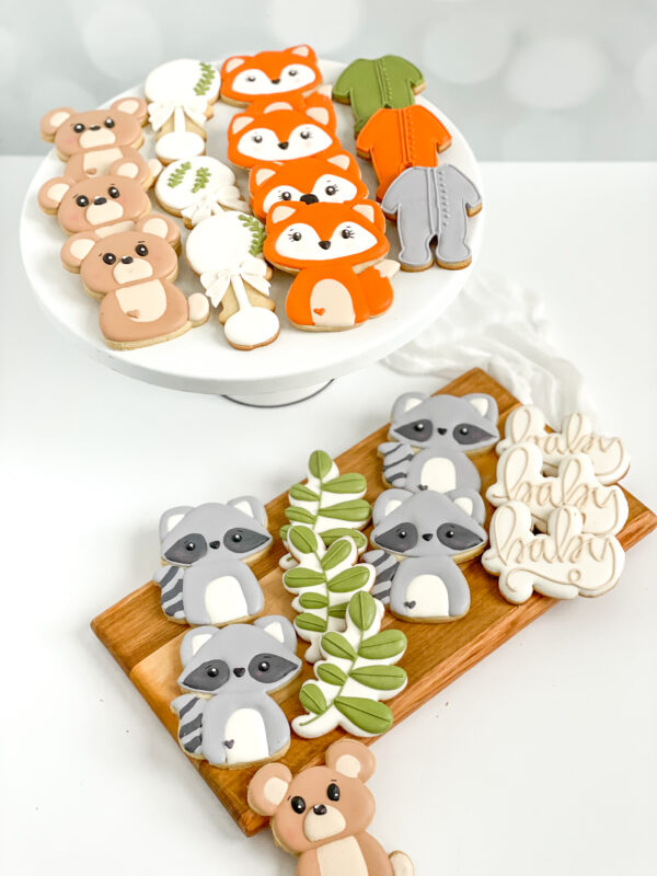 Decorated woodland baby shower cookies featuring adorable fox, bear, and raccoon cookies, leafy branch designs, baby onesies, and personalized “baby” script cookies in warm orange, brown, green, and soft gray icing. Decorated woodland baby shower cookies featuring adorable fox, bear, and raccoon cookies, leafy branch designs, baby onesies, and personalized “baby” script cookies in warm orange, brown, green, and soft gray icing.