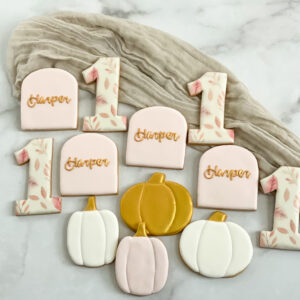 Custom fall first birthday sugar cookies decorated with pumpkins, autumn leaves, gold details, and personalized birthday cookies in soft blush, white, and warm fall colors.